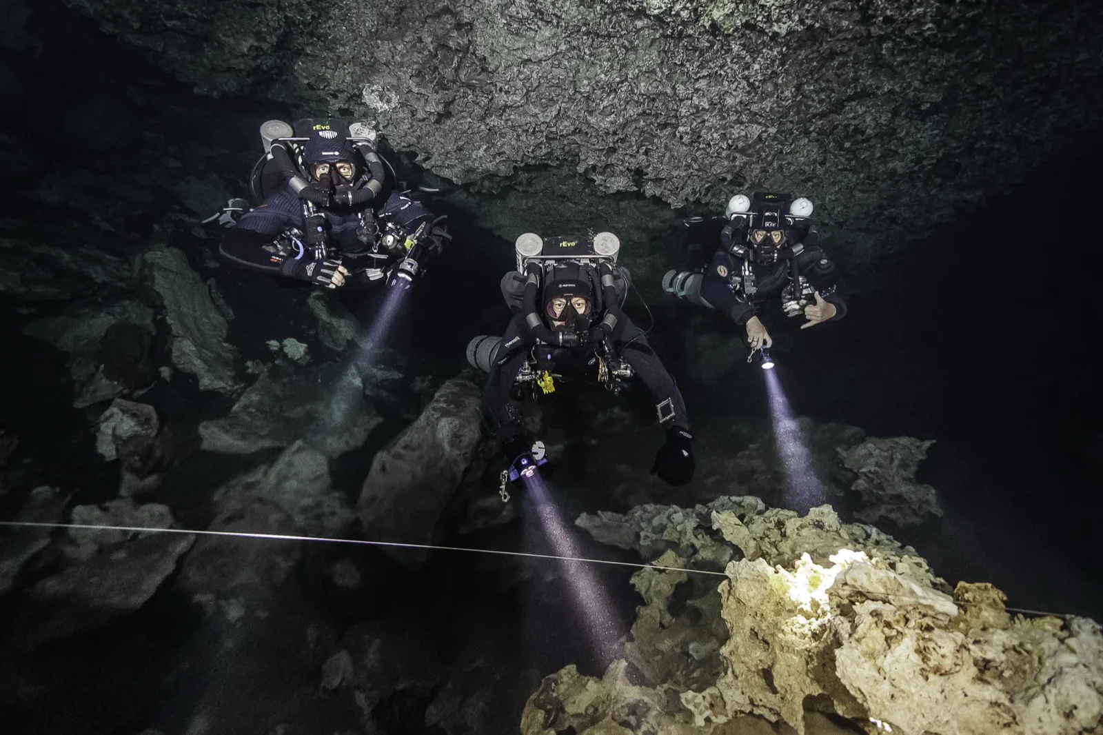 Three rEvo closed-circuit rebreather divers following the guideline through a Riviera Maya cave system
