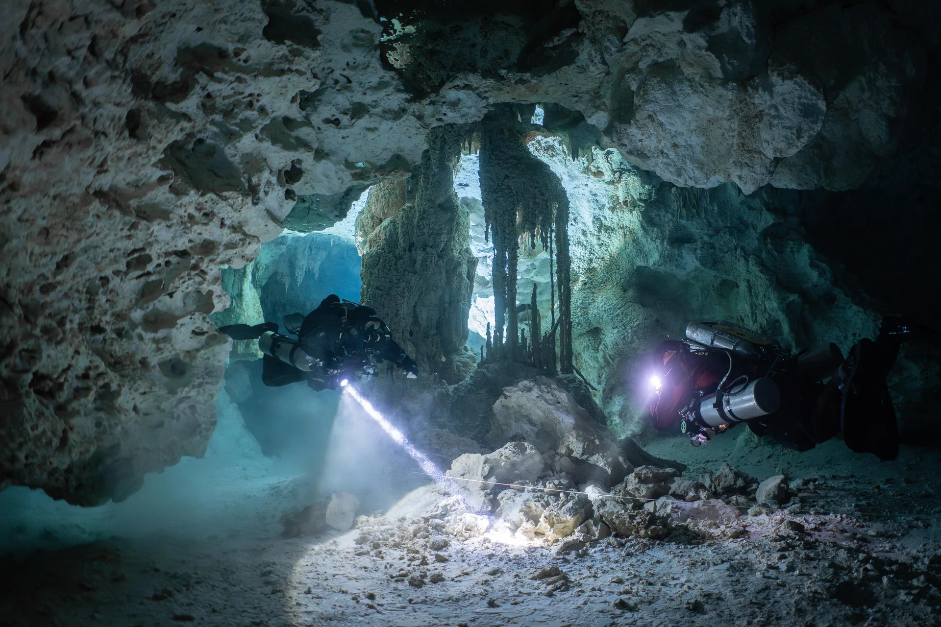 Zwei Taucher in Sidemount-Konfiguration folgen der Führungsleine durch eine Höhlenkammer mit Stalaktiten