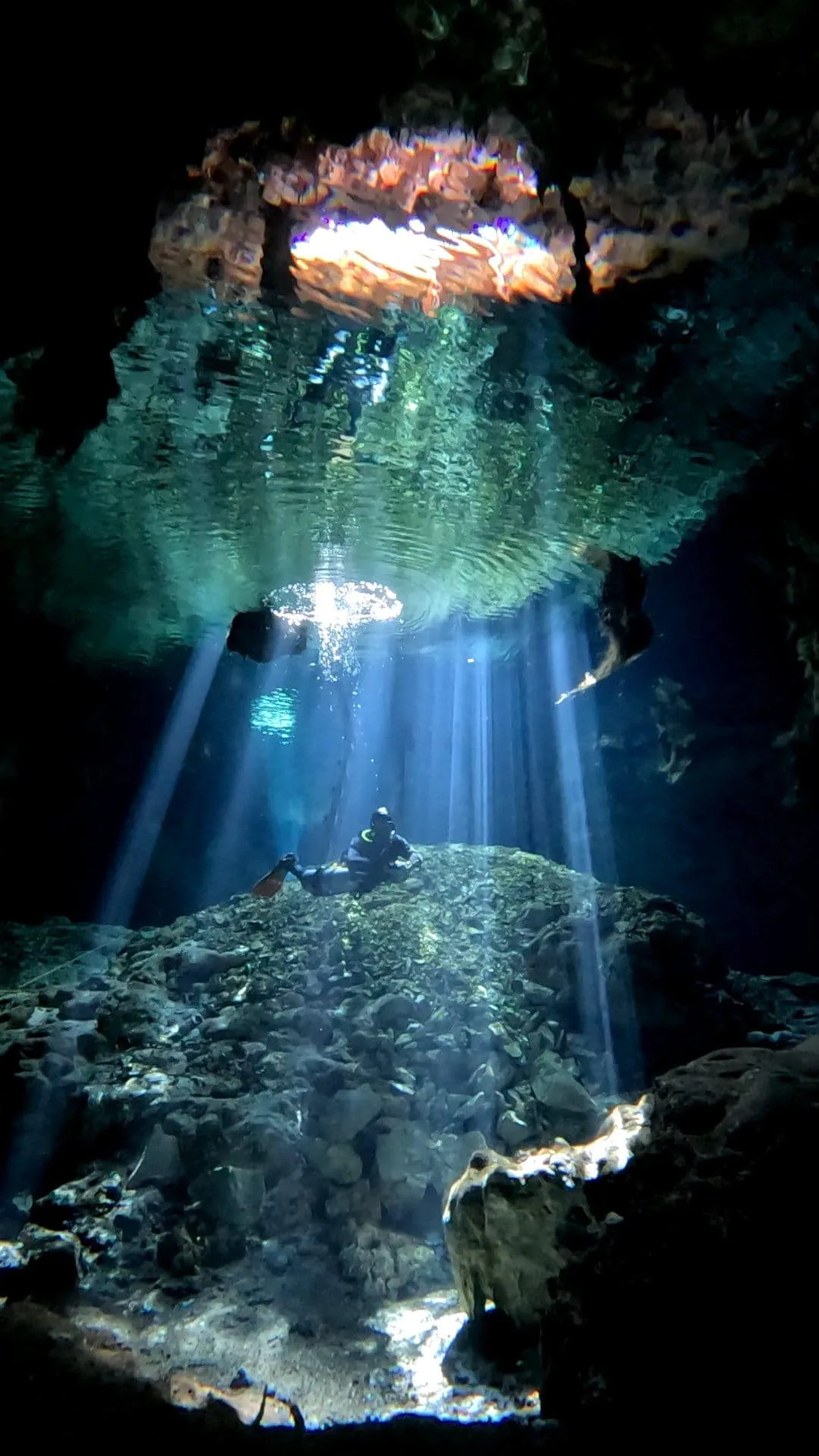 Cenote interior with sunlight column piercing the roof opening and a diver below