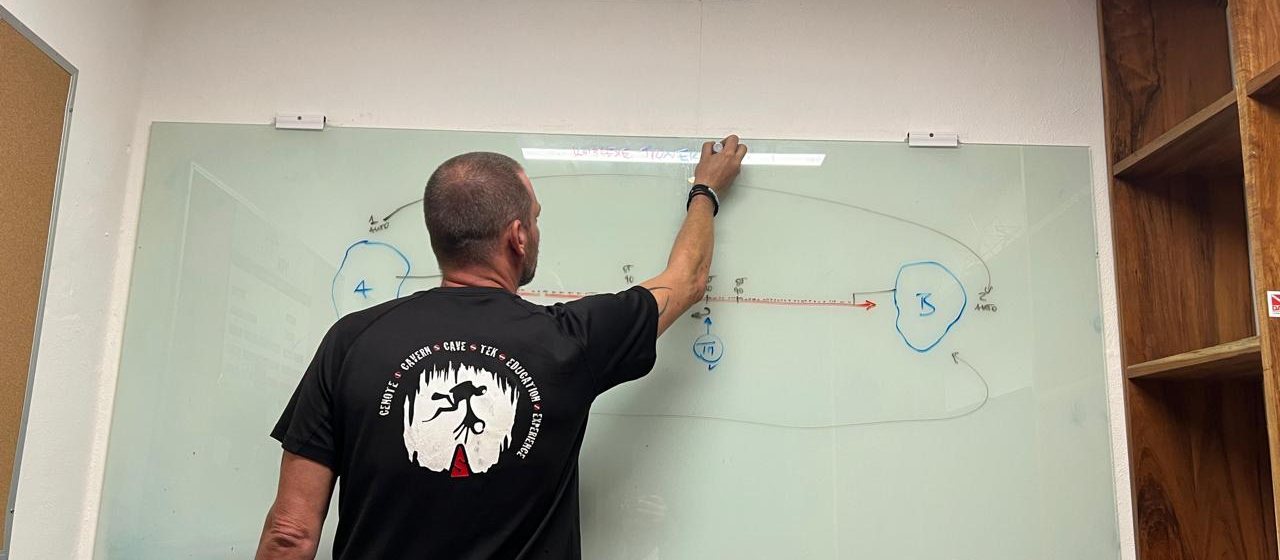 Theorieunterricht am Whiteboard: ein Taucher zeichnet ein Hoehlentauchprofil mit Gasmengen und Umkehrpunkt